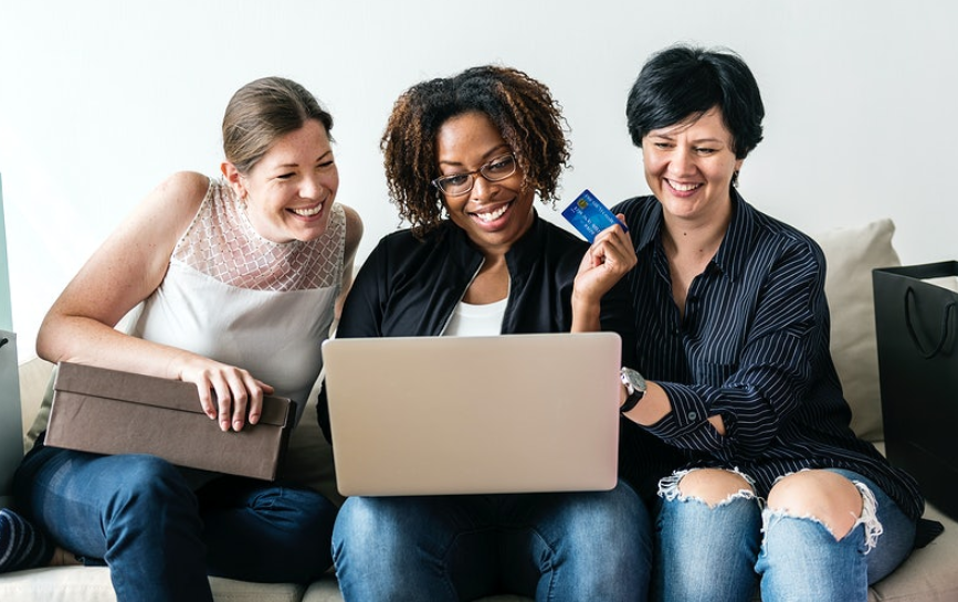 three woman looking at the laptop and holding a card 